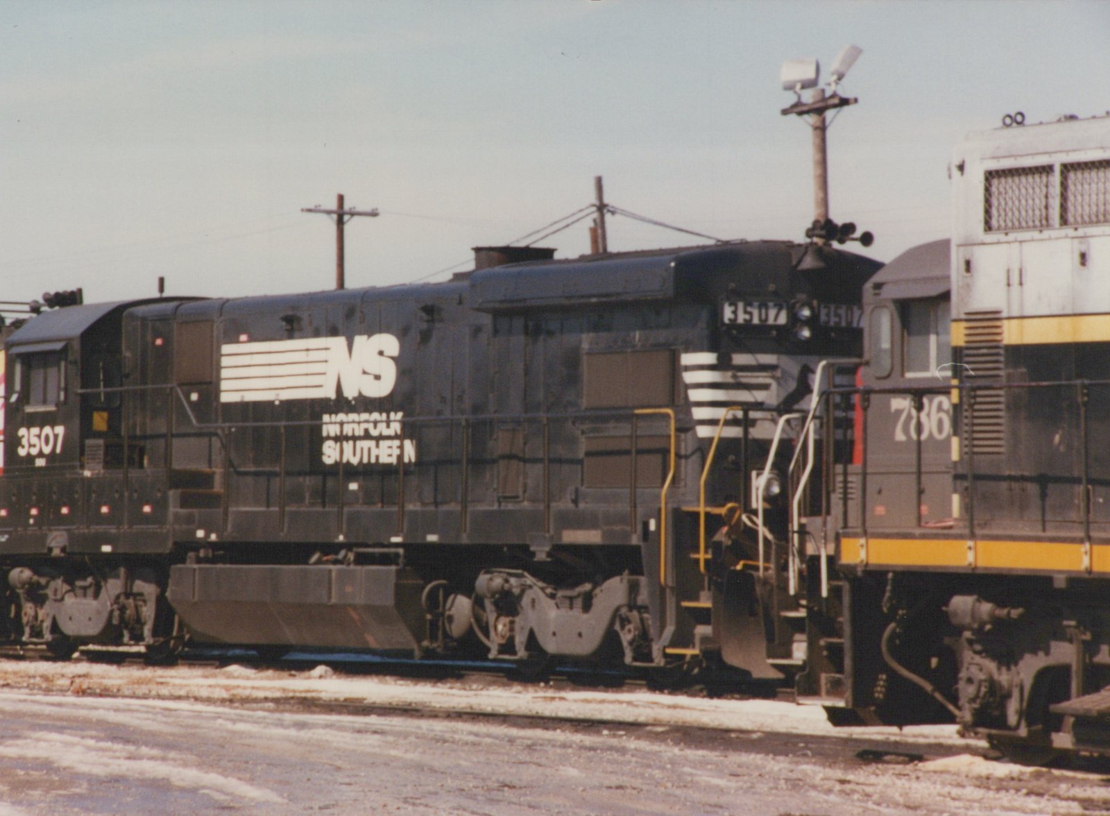 A black Norfolk Southern locomotive numbered 3507 is parked beside another locomotive in a snowy railroad yard, with the number 786 visible on the adjacent unit.