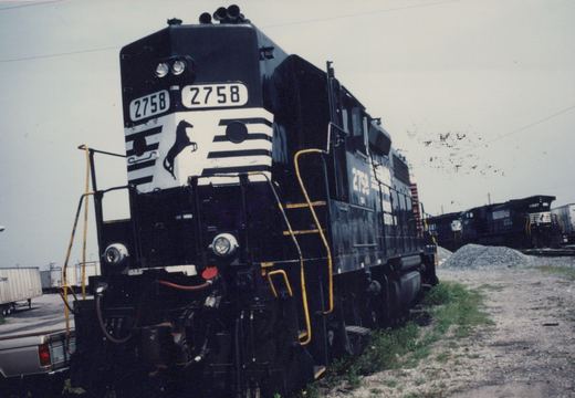 A black and white striped Norfolk Southern diesel locomotive, number 2758, is shown from a three-quarter front angle in a railroad yard.