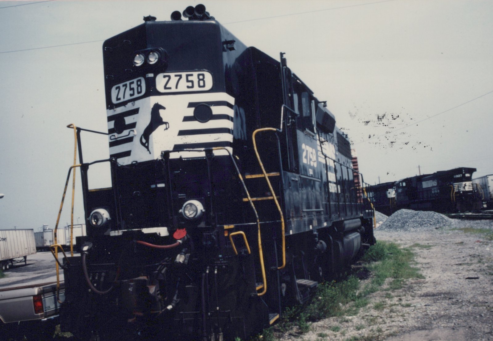 A black and white striped Norfolk Southern diesel locomotive, number 2758, is shown from a three-quarter front angle in a railroad yard.