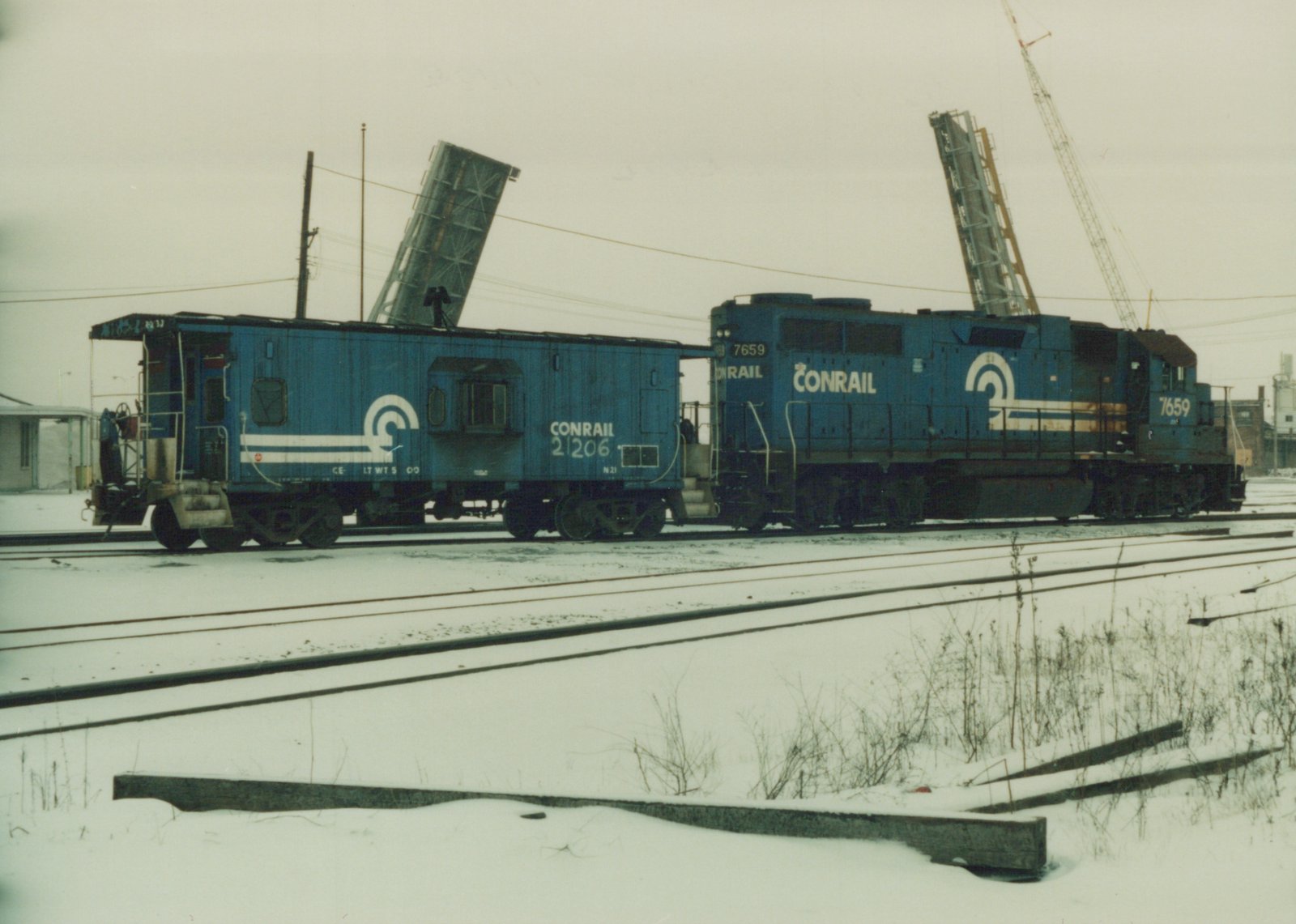 Two blue Conrail railroad vehicles, a locomotive numbered 7659 and a caboose numbered 21206, on snow-covered tracks in a yard.