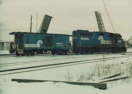 Two blue Conrail railroad vehicles, a locomotive numbered 7659 and a caboose numbered 21206, on snow-covered tracks in a yard.