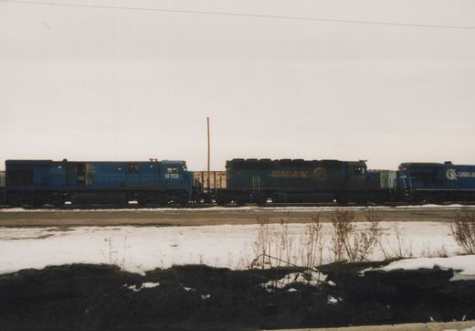 Three blue Conrail diesel locomotives, including numbers 6701 and 6490, sit on tracks in a snow-covered yard under an overcast sky.