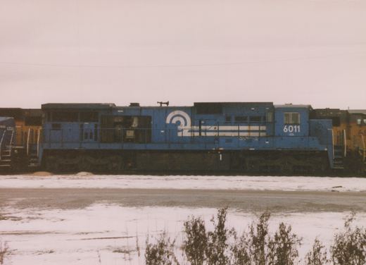 A side view of a blue Conrail diesel locomotive, number 6011, standing in a snowy yard with other locomotives partially visible in the background.