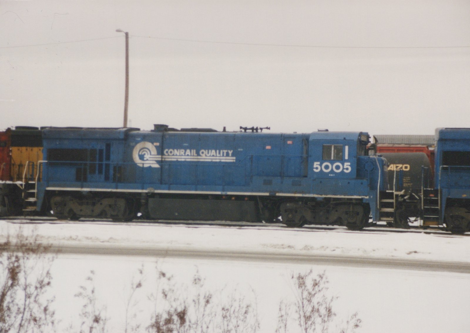 Side view of a blue Conrail diesel locomotive number 5005 in a snowy yard, with 'CONRAIL QUALITY' lettering on its side.