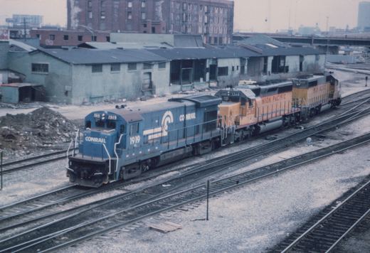 Two diesel locomotives, one blue Conrail and one yellow Union Pacific, on parallel tracks in a snowy industrial yard.