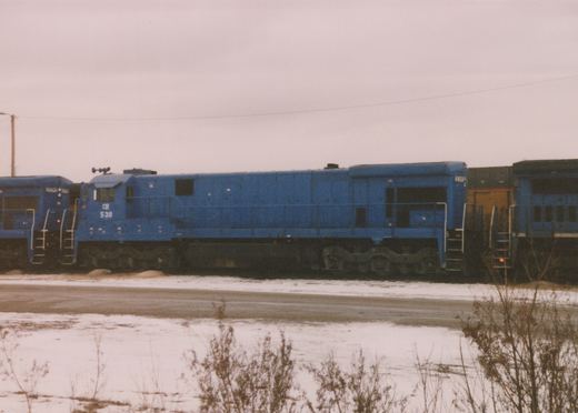 A side view of a blue Conrail diesel locomotive numbered 539 parked in a snow-covered yard with other locomotives nearby under an overcast sky.