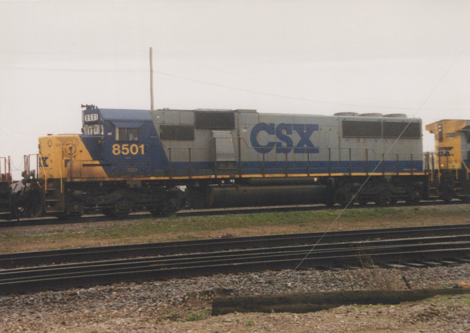 A CSX Transportation locomotive numbered 8501 sits on tracks in a yard under an overcast sky.