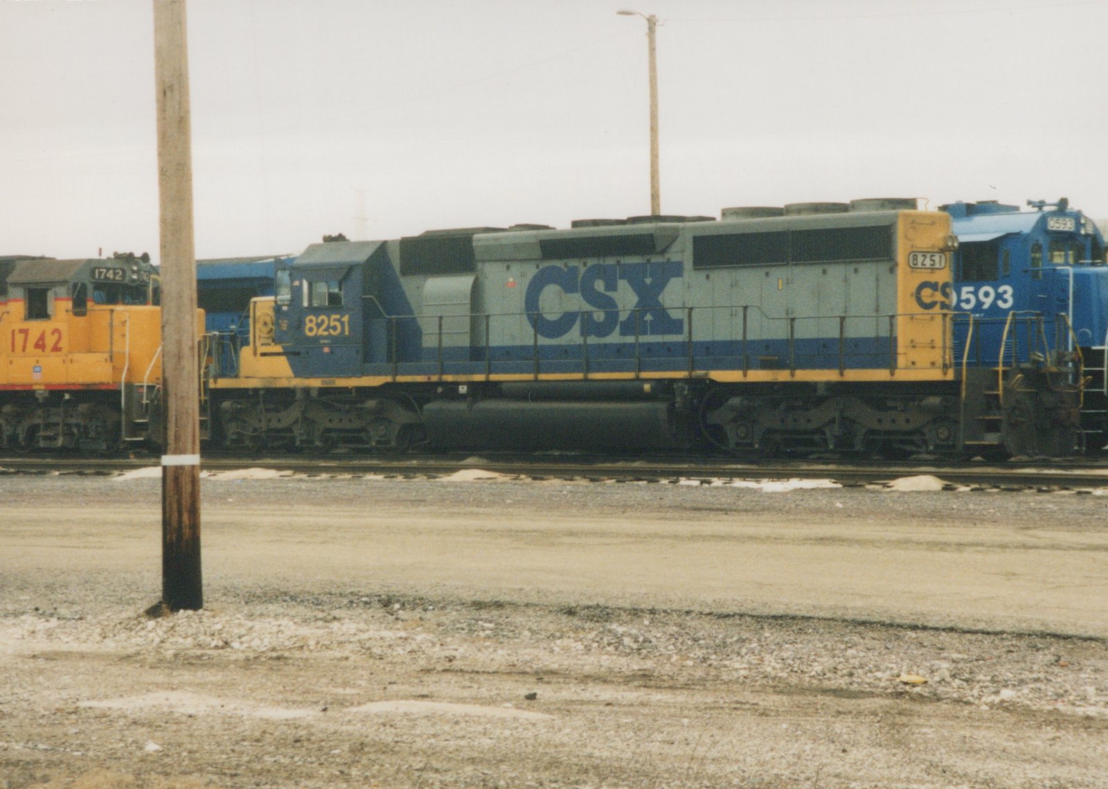 Side view of a blue and gray CSX locomotive numbered 8251 on a railroad track in a snowy yard, with other locomotives nearby.