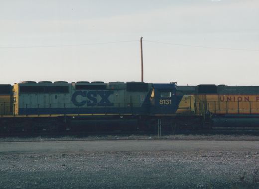 A side view of a CSX locomotive numbered 8131 in a rail yard, with a Union Pacific locomotive visible behind it.