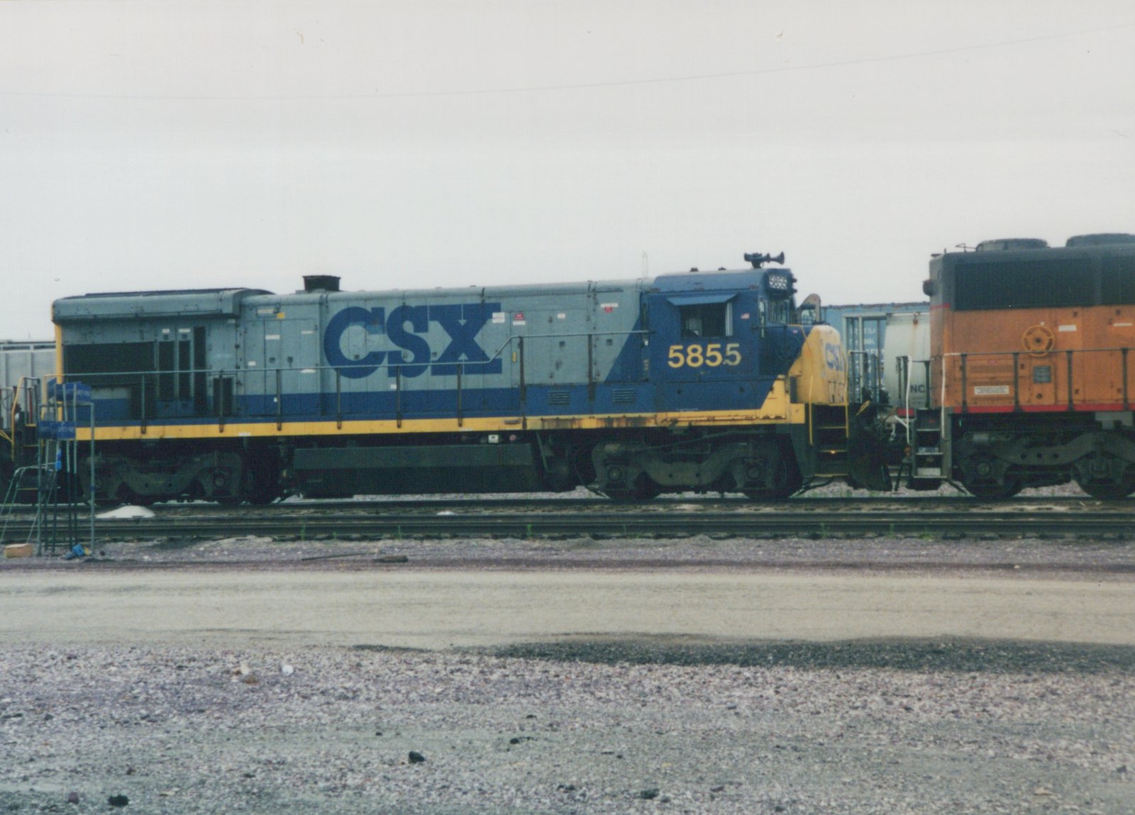 A blue, gray and yellow CSX locomotive number 5855 is parked on railroad tracks in a yard with another locomotive coupled behind it.