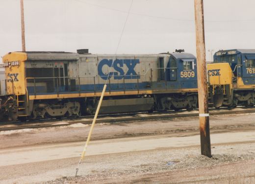Two CSX locomotives, numbers 5809 and 7615, are parked on parallel tracks in a snowy yard with utility poles and gravel ground.