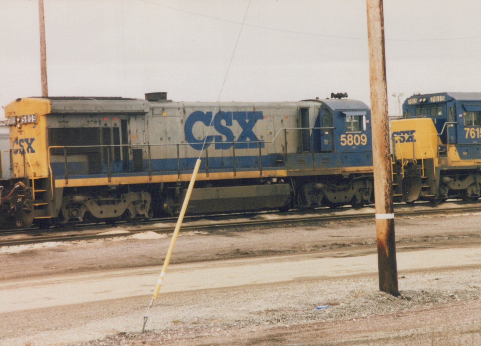 Two CSX locomotives, numbers 5809 and 7615, are parked on parallel tracks in a snowy yard with utility poles and gravel ground.