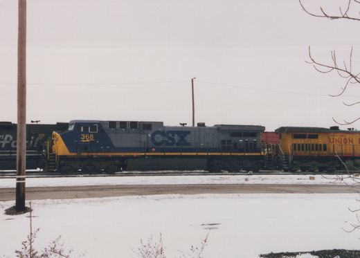 A CSX locomotive numbered 368 and a Union Pacific locomotive parked side by side on a snowy railroad yard.