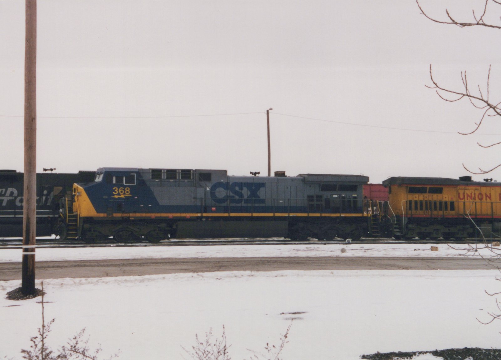 A CSX locomotive numbered 368 and a Union Pacific locomotive parked side by side on a snowy railroad yard.