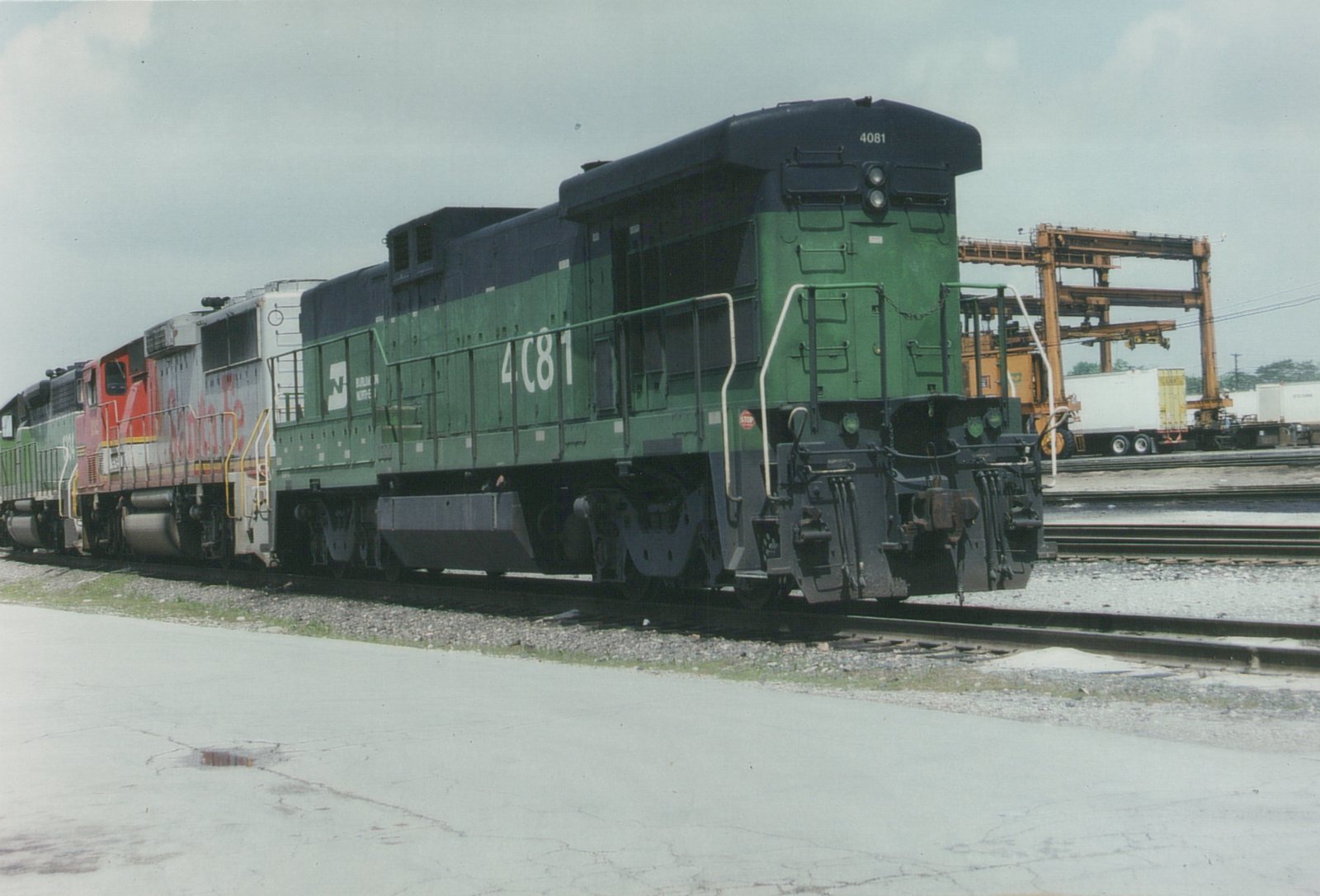 Two diesel locomotives, one green and black with number 4081 for Burlington Northern, and one red and silver with Santa Fe lettering, are parked on parallel tracks in a rail yard.