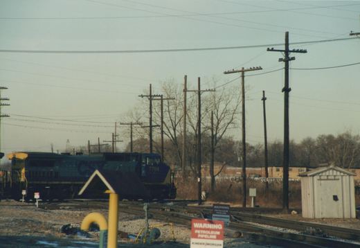 A CSX Transportation diesel locomotive, number 7784, is parked on railroad tracks in a winter setting with bare trees and utility poles in the background.