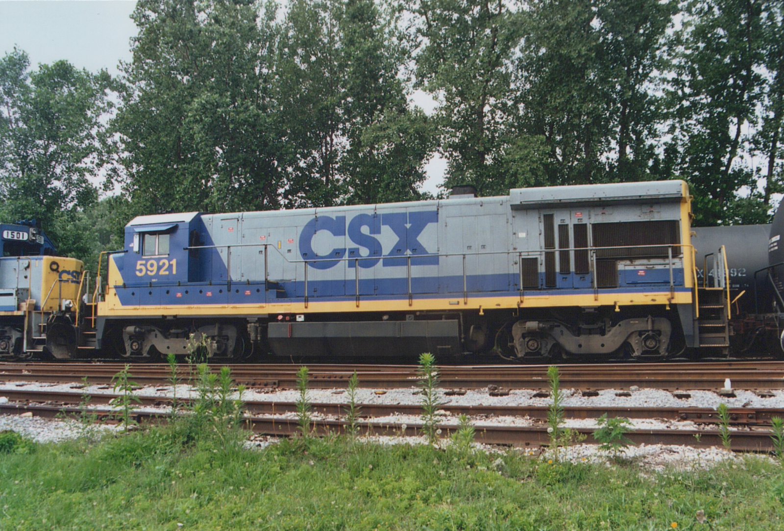 A side view of a blue, gray and yellow CSX locomotive with the number 5921, parked on railroad tracks with trees in the background.