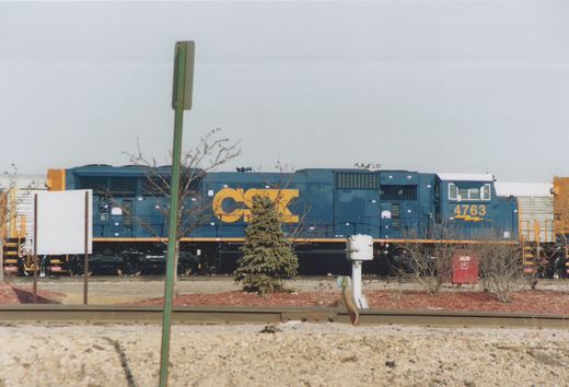 A blue and yellow CSX locomotive with the number 4763 on the cab side, seen from the side with bare trees and a cloudy sky in the background.