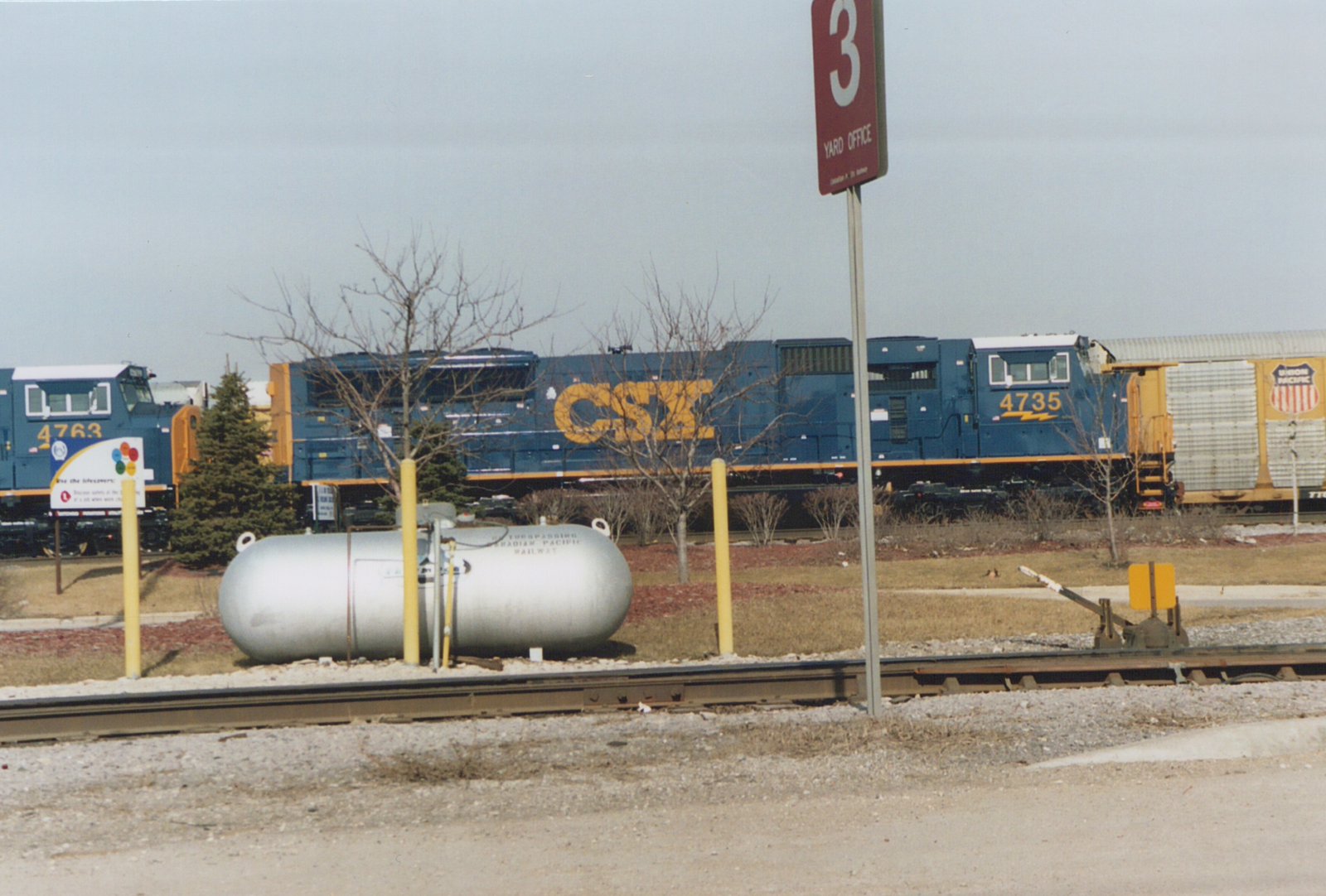 A blue and yellow CSX train with locomotive number 4735 is seen in a rail yard during winter, with another CSX engine and a Union Pacific car nearby.