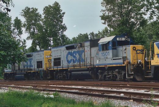 Two CSX diesel locomotives, numbers 1501 and 1518, are parked side by side on parallel tracks in a yard with trees in the background.