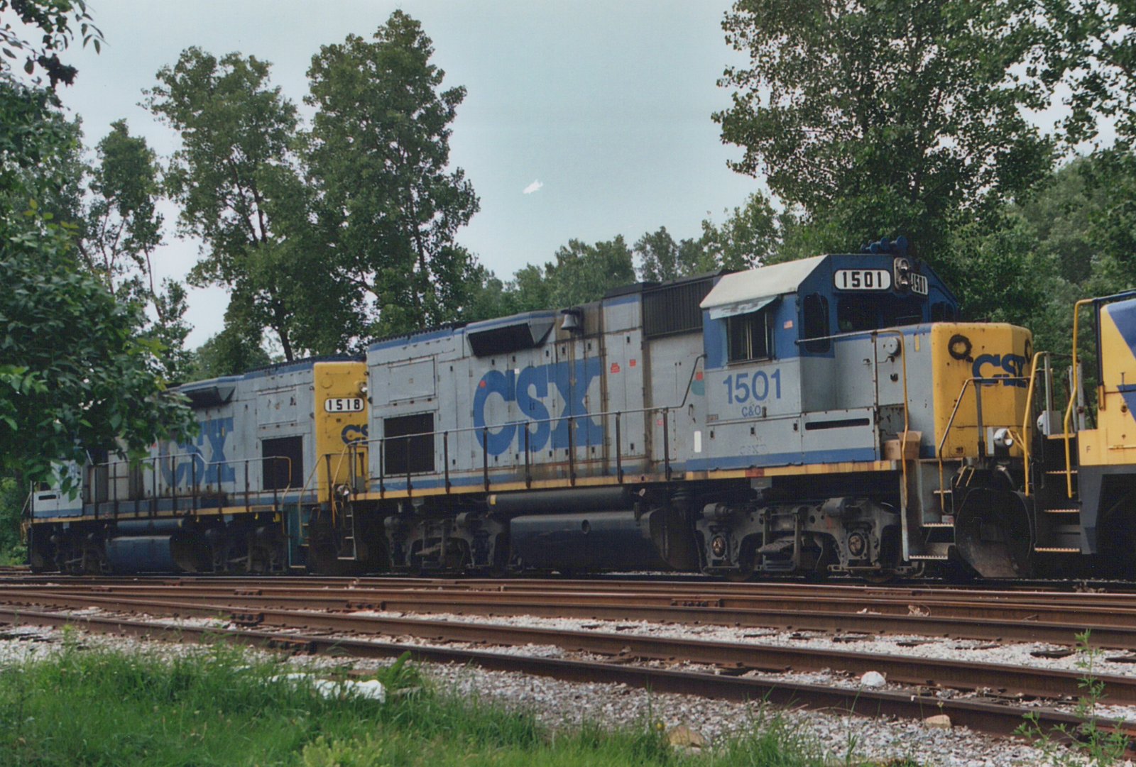 Two CSX diesel locomotives, numbers 1501 and 1518, are parked side by side on parallel tracks in a yard with trees in the background.