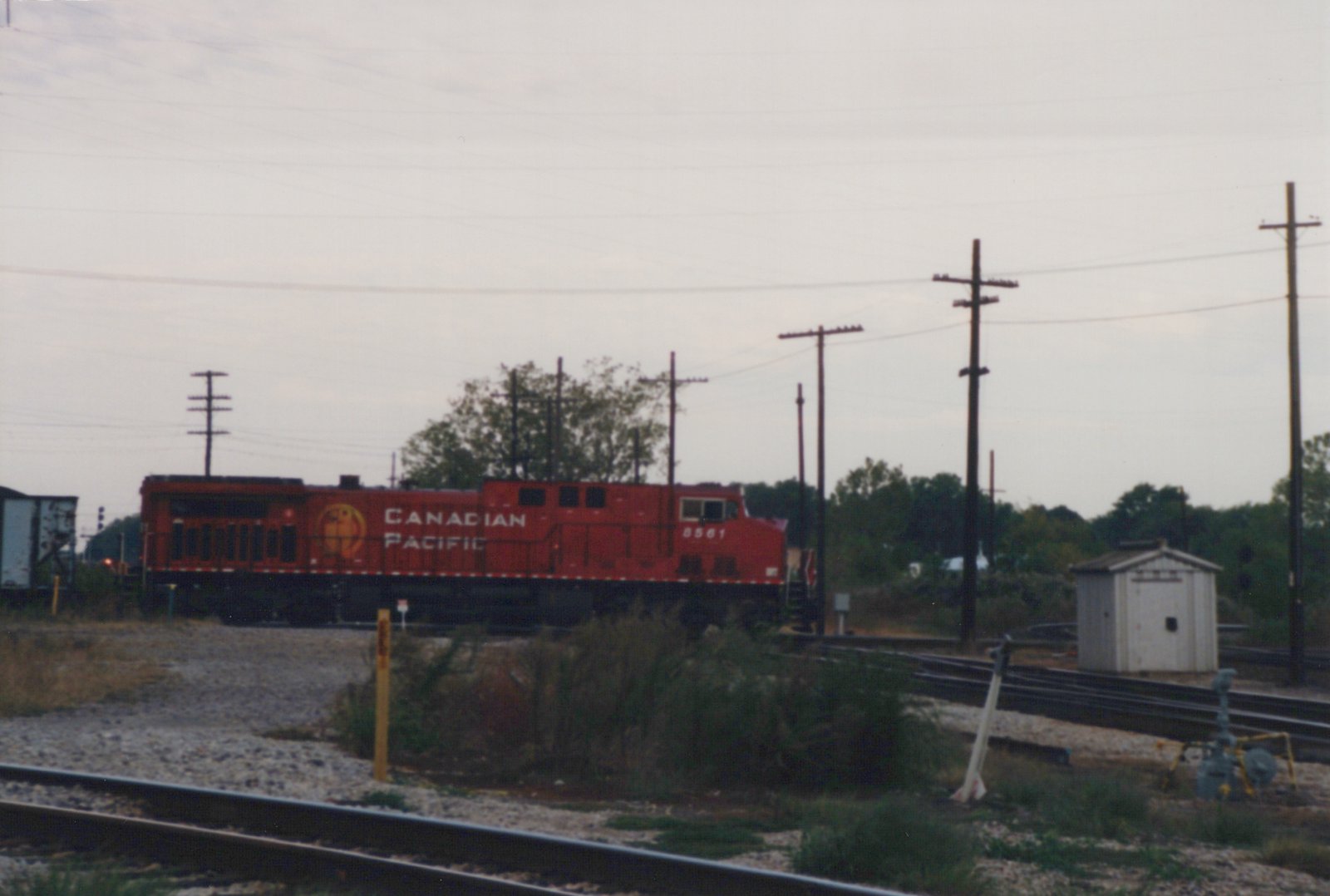 A side view of a red Canadian Pacific diesel locomotive, number 8561, on a set of train tracks with utility poles and trees in the background.