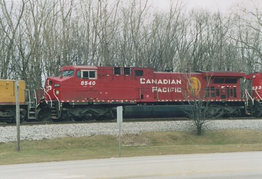 A red Canadian Pacific diesel locomotive numbered 8540 is shown on a railroad track with bare trees in the background.