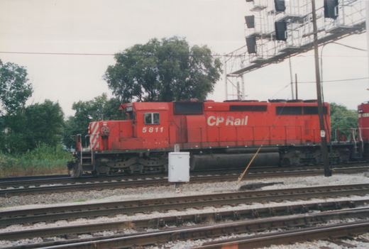 A red Canadian Pacific diesel locomotive numbered 5811 is on a set of railroad tracks, with another matching locomotive partially visible behind it, under an overcast sky.