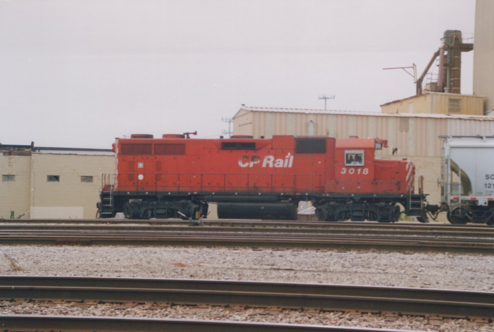 A red locomotive with 'CP Rail' on its side, numbered 3018, is on railroad tracks next to industrial buildings.