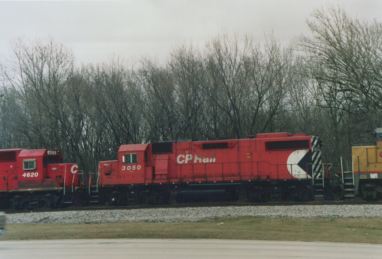 Two red Canadian Pacific diesel locomotives, numbered 3050 and 4620, sit side-by-side on a gravel track with bare trees in the background under an overcast sky.