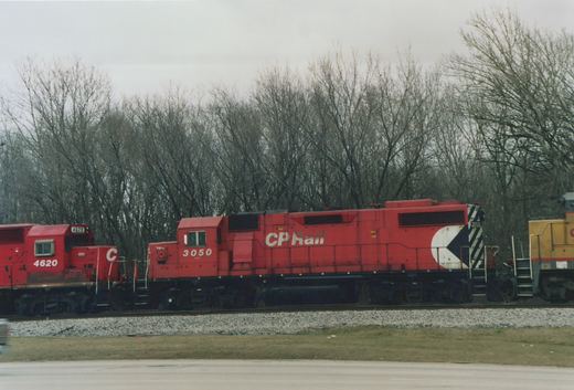 Two red Canadian Pacific diesel locomotives, numbered 3050 and 4620, sit side-by-side on a gravel track with bare trees in the background under an overcast sky.
