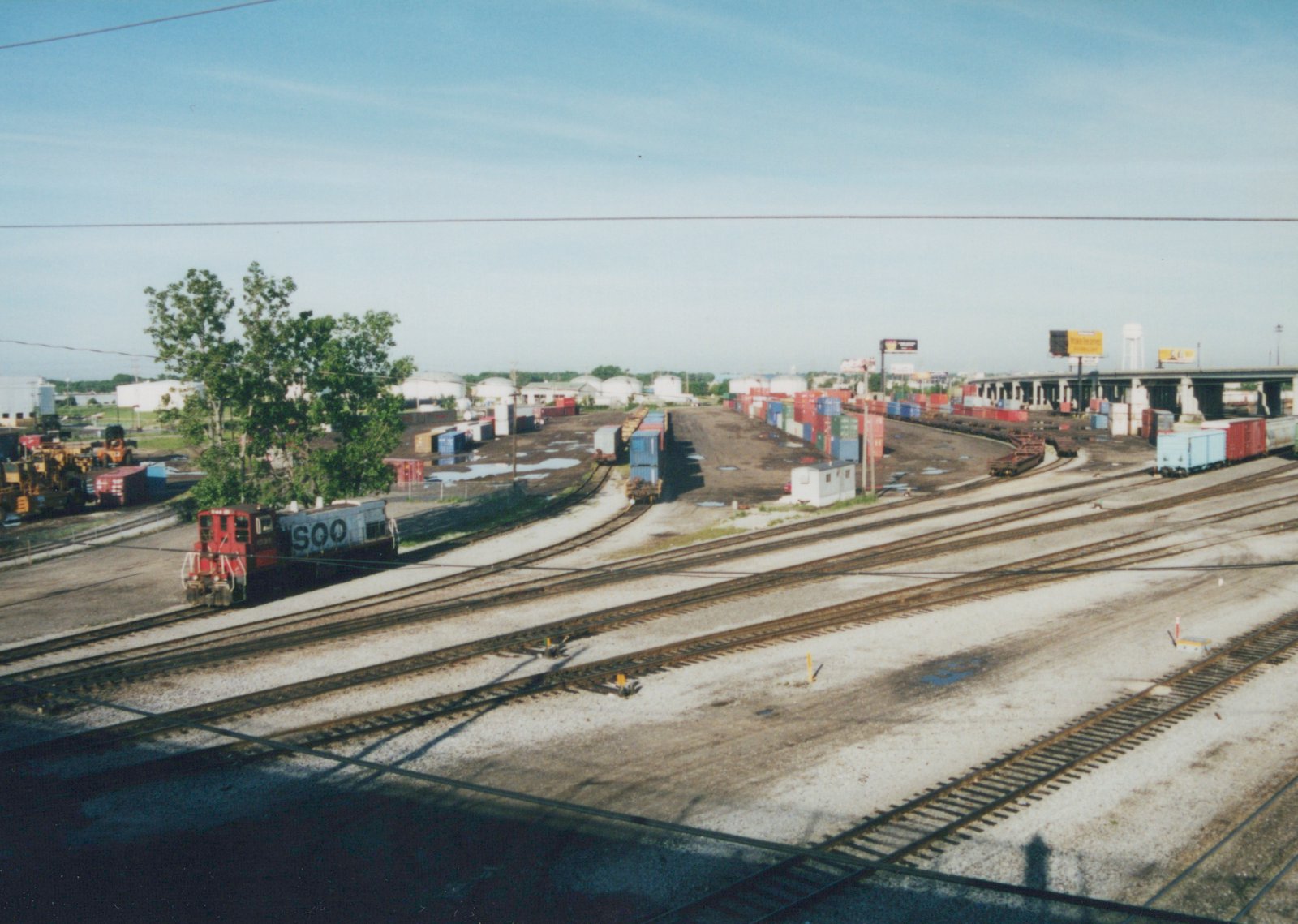 An elevated view of a Soo Line SW1200 locomotive moving through a sprawling rail yard filled with freight cars and shipping containers, located in Franklin Park, Illinois.