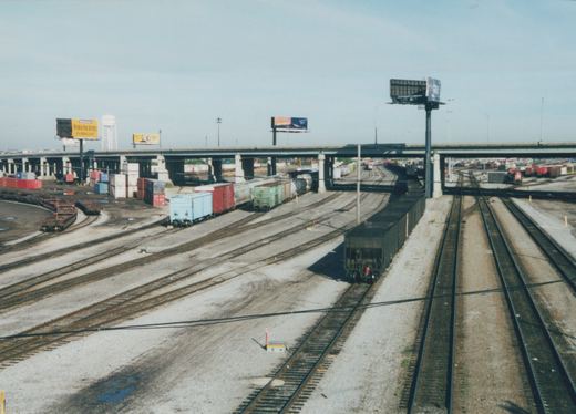 A high-angle view of a sprawling railroad yard with dozens of tracks, freight cars, and an overpass, located in Franklin Park, Illinois.