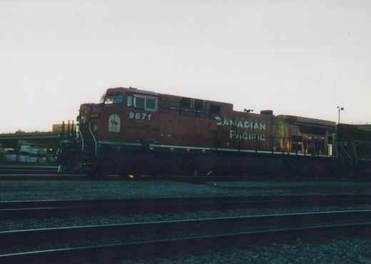 Side view of a red Canadian Pacific diesel locomotive numbered 9671 in a rail yard at dusk, with a second locomotive numbered 8522 behind it.