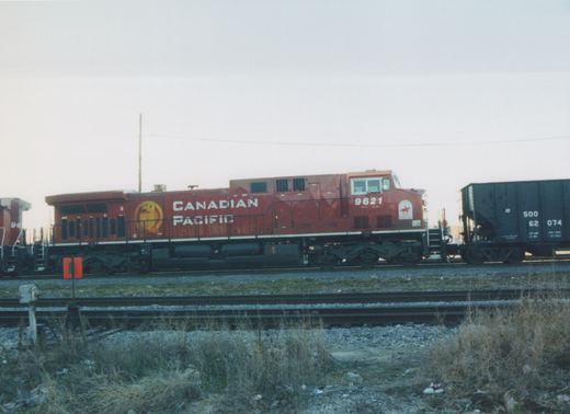 Side view of a red Canadian Pacific diesel locomotive, number 9621, standing on tracks in a yard with a black freight car nearby.