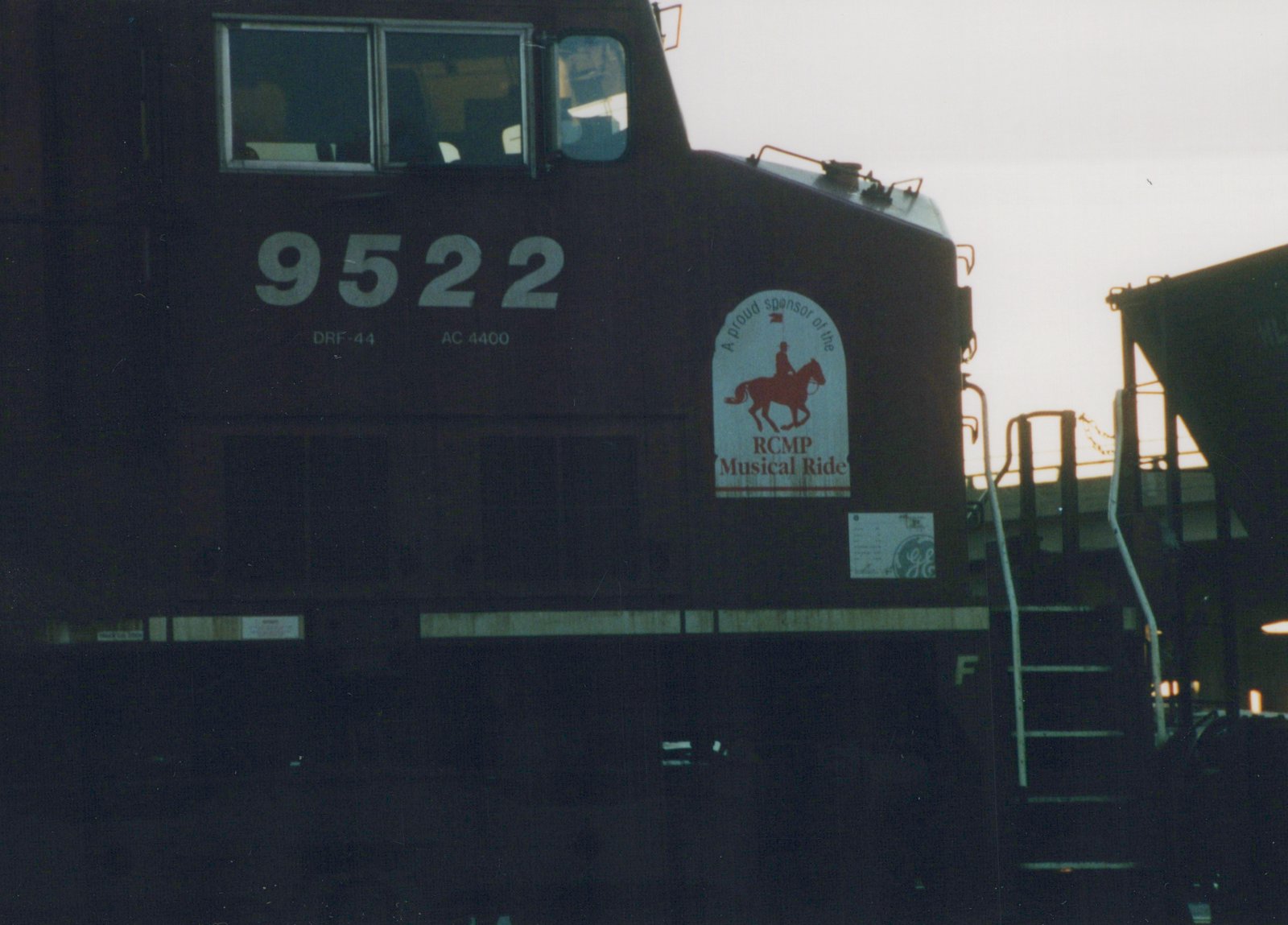 A close-up of a dark-colored Canadian Pacific locomotive numbered 9522, with a decal for the RCMP Musical Ride on its side, set in a yard during dusk with overcast lighting.