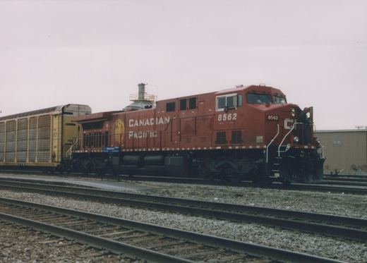 A red Canadian Pacific diesel locomotive with the number 8562 is parked on the tracks next to a yellow freight car, with a person standing on the locomotive's platform.