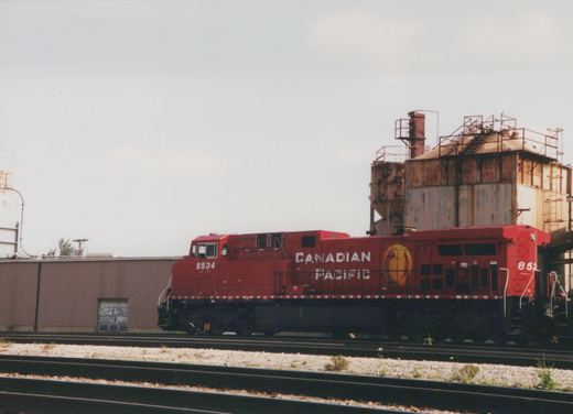 A red Canadian Pacific diesel locomotive, number 8534, is parked on a set of tracks next to an industrial building under an overcast sky.