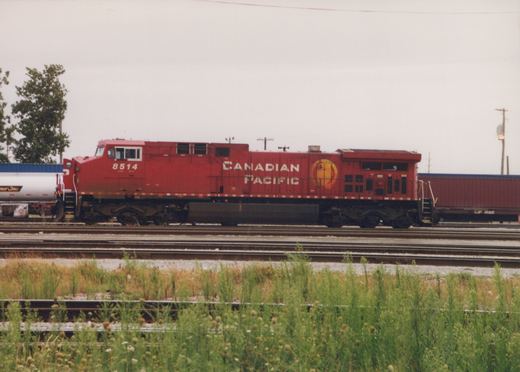 A red Canadian Pacific locomotive, number 8514, is parked on a set of railroad tracks. The locomotive's side has white lettering and a yellow logo. There are freight cars behind it and grass in the foreground.