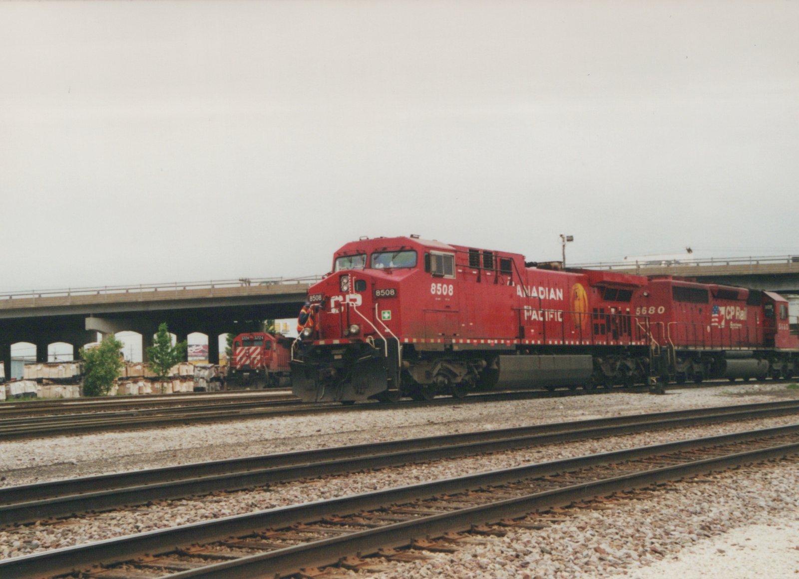 A red Canadian Pacific freight train with locomotive 8508 leading, followed by locomotive 5680, on tracks under a concrete overpass on a cloudy day.