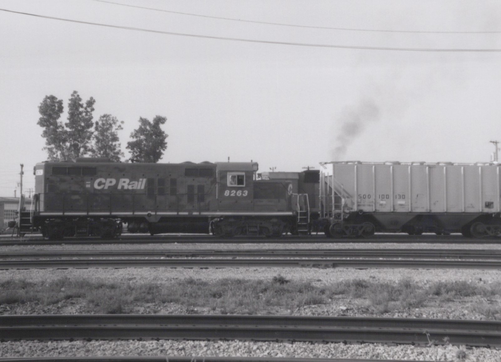 Black and white photo of a Canadian Pacific SD40 locomotive numbered 8263, pulling a covered hopper car on a railroad yard track under an overcast sky.