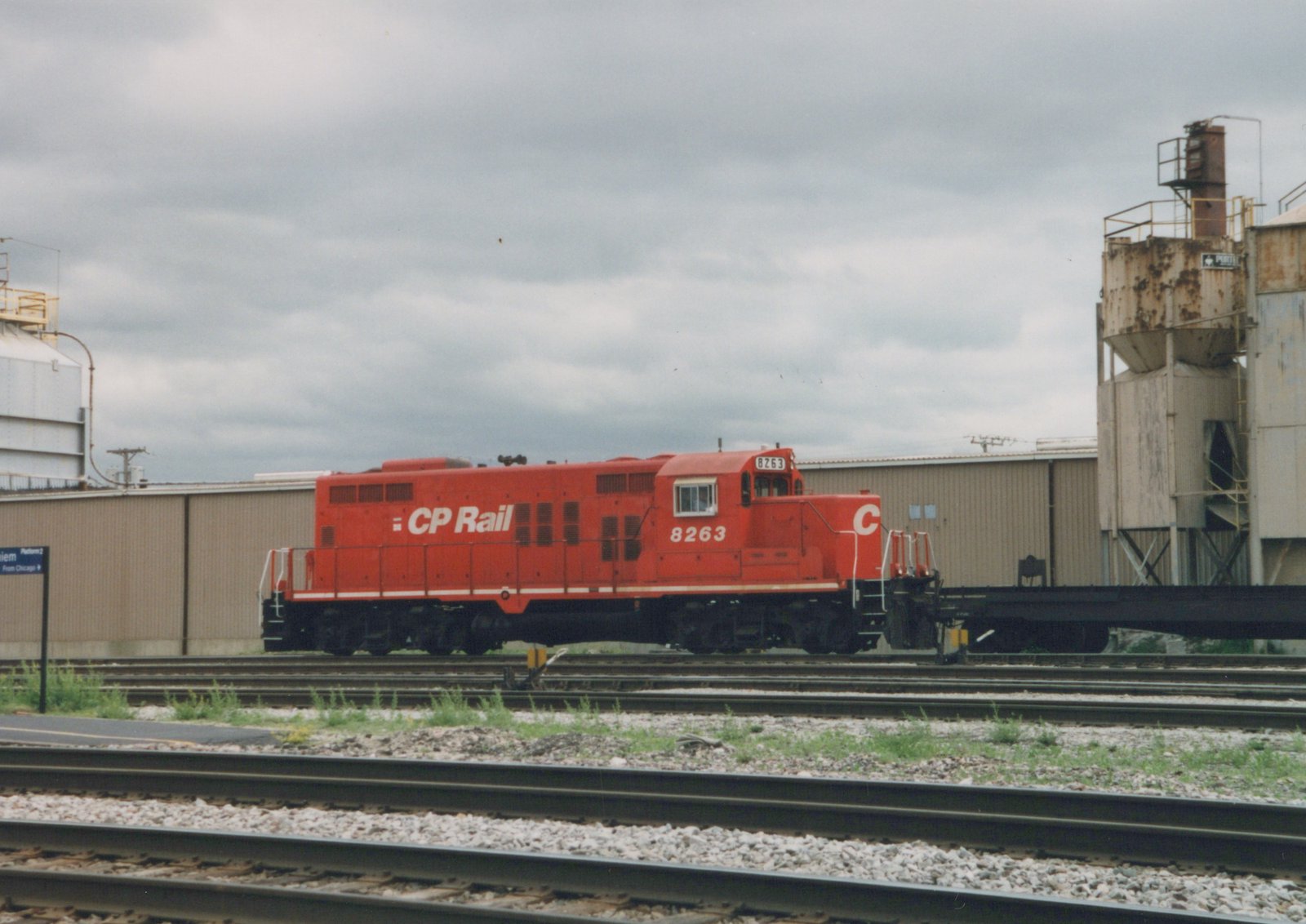 A red CP Rail diesel locomotive, number 8263, is parked on tracks in a yard with industrial buildings in the background under a cloudy sky.