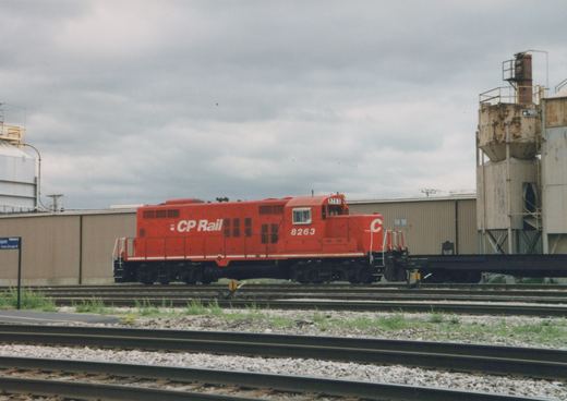 A red CP Rail diesel locomotive, number 8263, is parked on tracks in a yard with industrial buildings in the background under a cloudy sky.