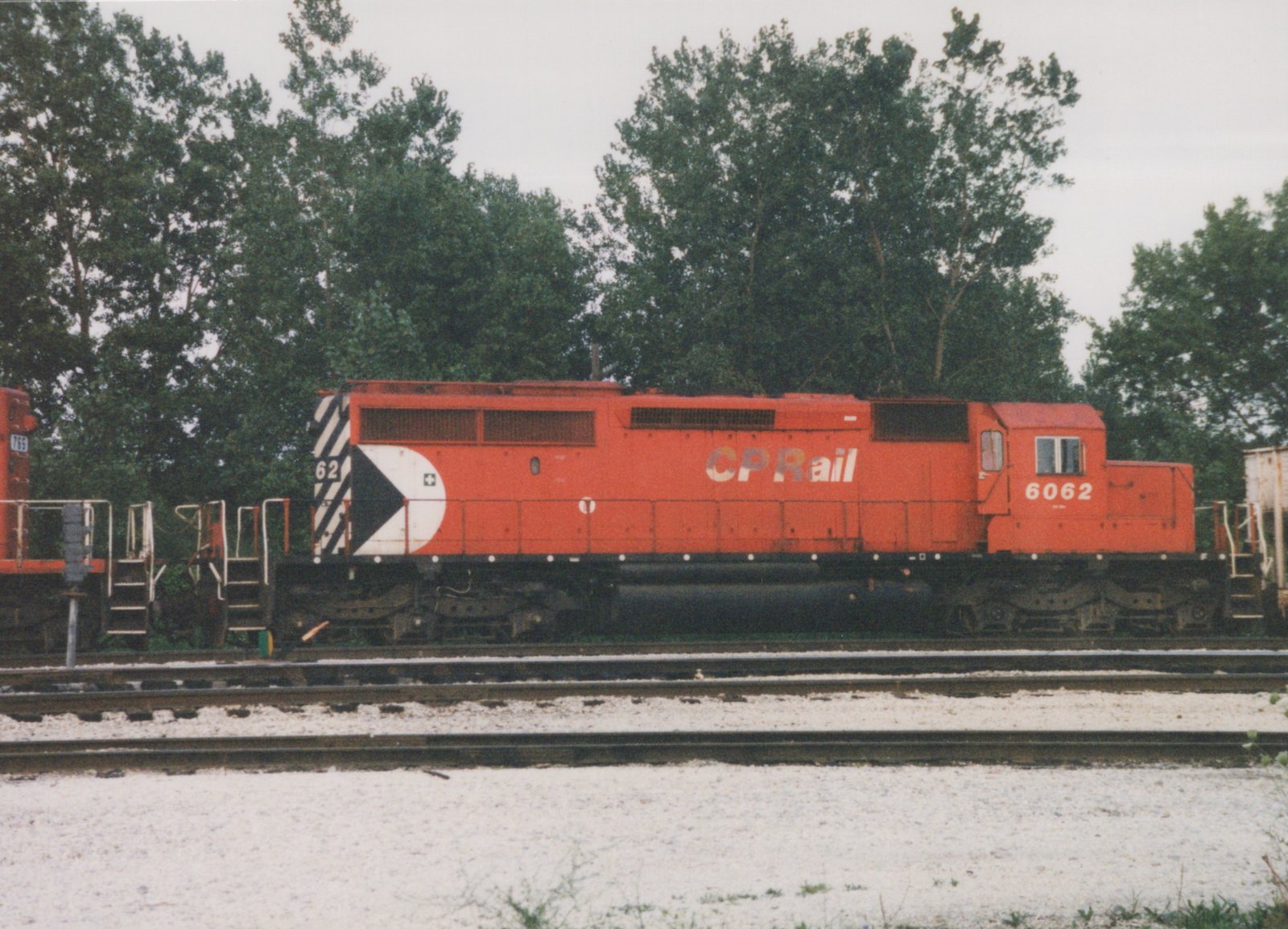 Side view of a red Canadian Pacific locomotive, number 6062, parked on tracks in a yard with trees in the background.