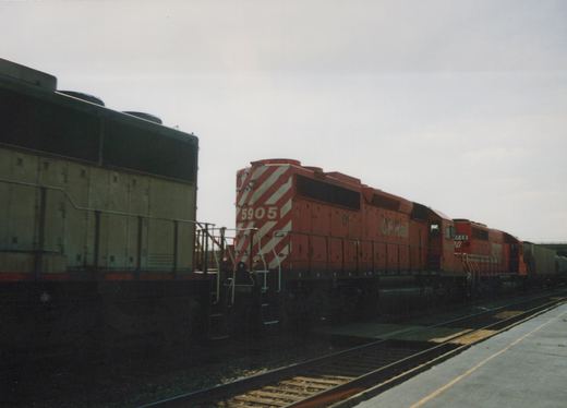 Two red CP Rail diesel locomotives, numbered 5905 and 5908, are parked on tracks beside a station platform under an overcast sky.