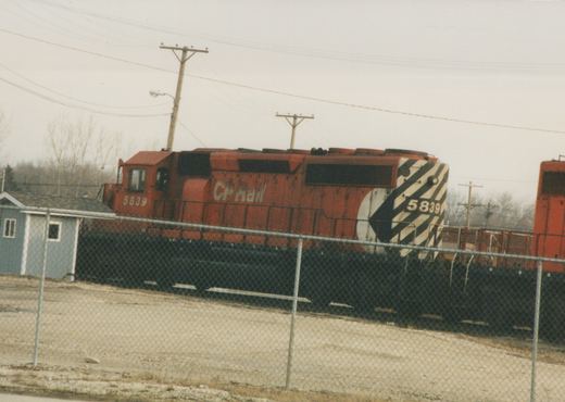 A red CP Rail diesel locomotive numbered 5839 is seen from a three-quarter front view, behind a chain-link fence in a yard on an overcast winter day.