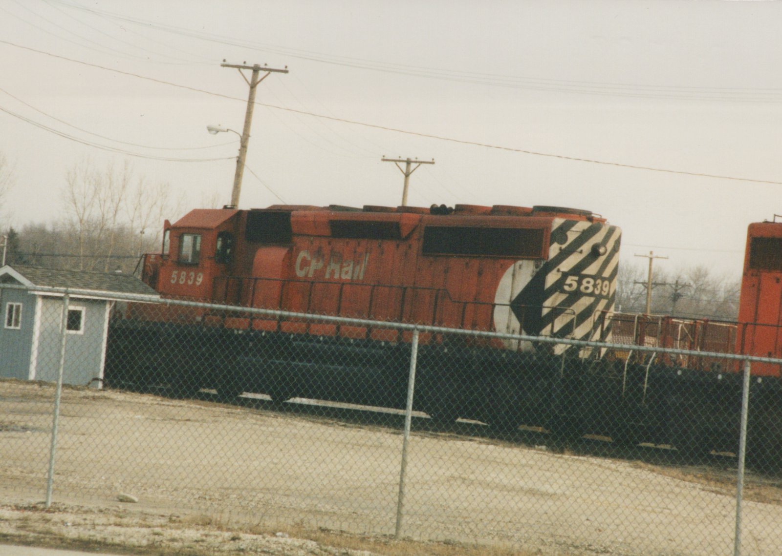 A red CP Rail diesel locomotive numbered 5839 is seen from a three-quarter front view, behind a chain-link fence in a yard on an overcast winter day.