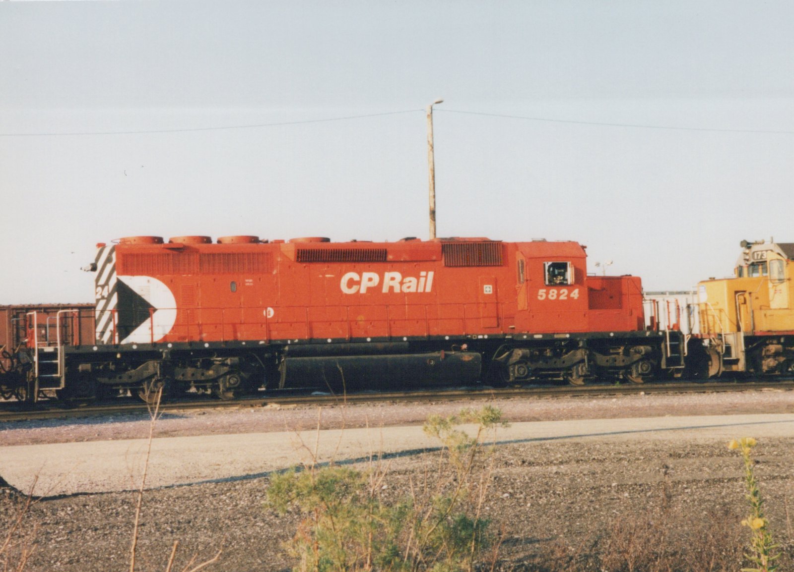 A red CP Rail diesel locomotive numbered 5824 sits on a track in a rail yard with another yellow locomotive in the background.