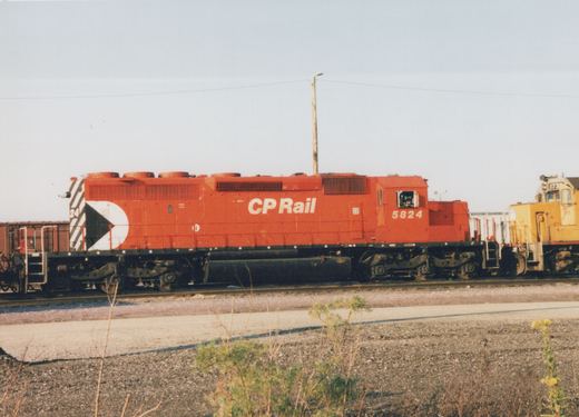A red CP Rail diesel locomotive numbered 5824 sits on a track in a rail yard with another yellow locomotive in the background.