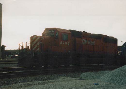 A side view of an orange CP Rail locomotive numbered 5793 on railroad tracks in a gravel yard under a cloudy sky.